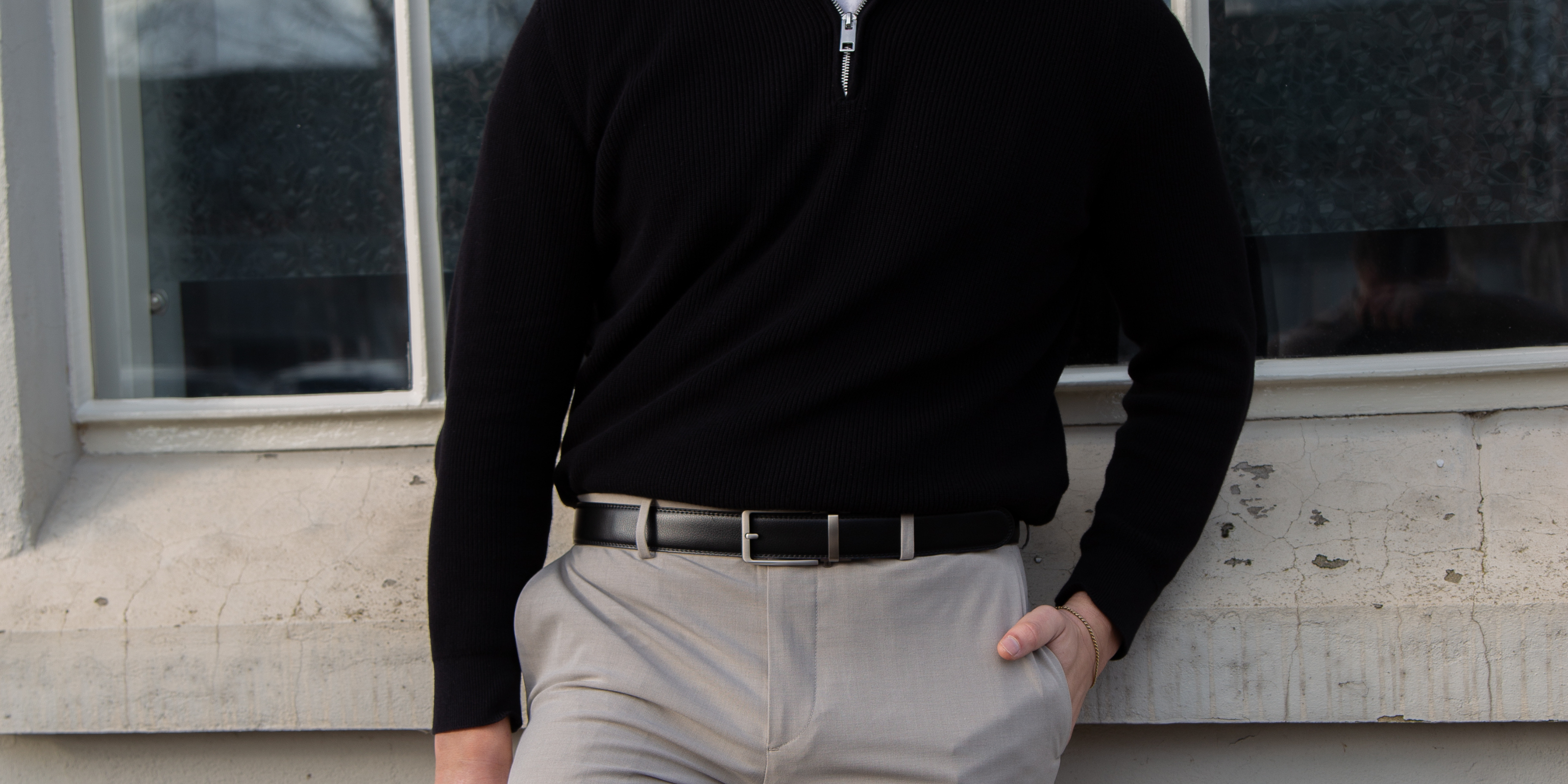 Een model leunt casual tegen een muur en draagt de zwarte Buckle Up-riem, wat zorgt voor een moderne en stoere uitstraling.